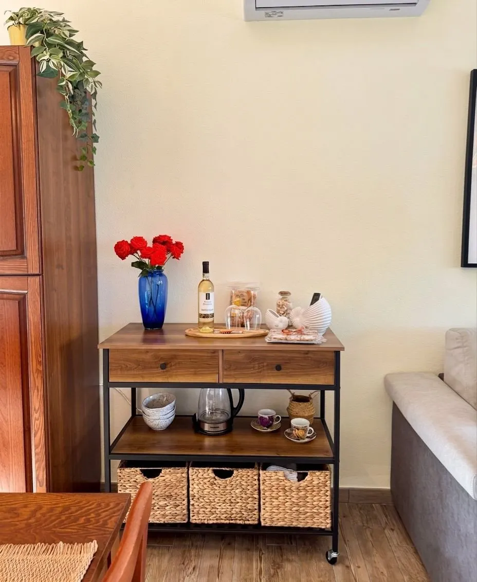 Kit di benvenuto della suite a Cagliari: bottiglia di vino bianco sardo aperta, bicchieri sul vassoio, garofani rossi freschi in vaso blu cobalto, caffettiera e tazzine in ceramica artigianale.
