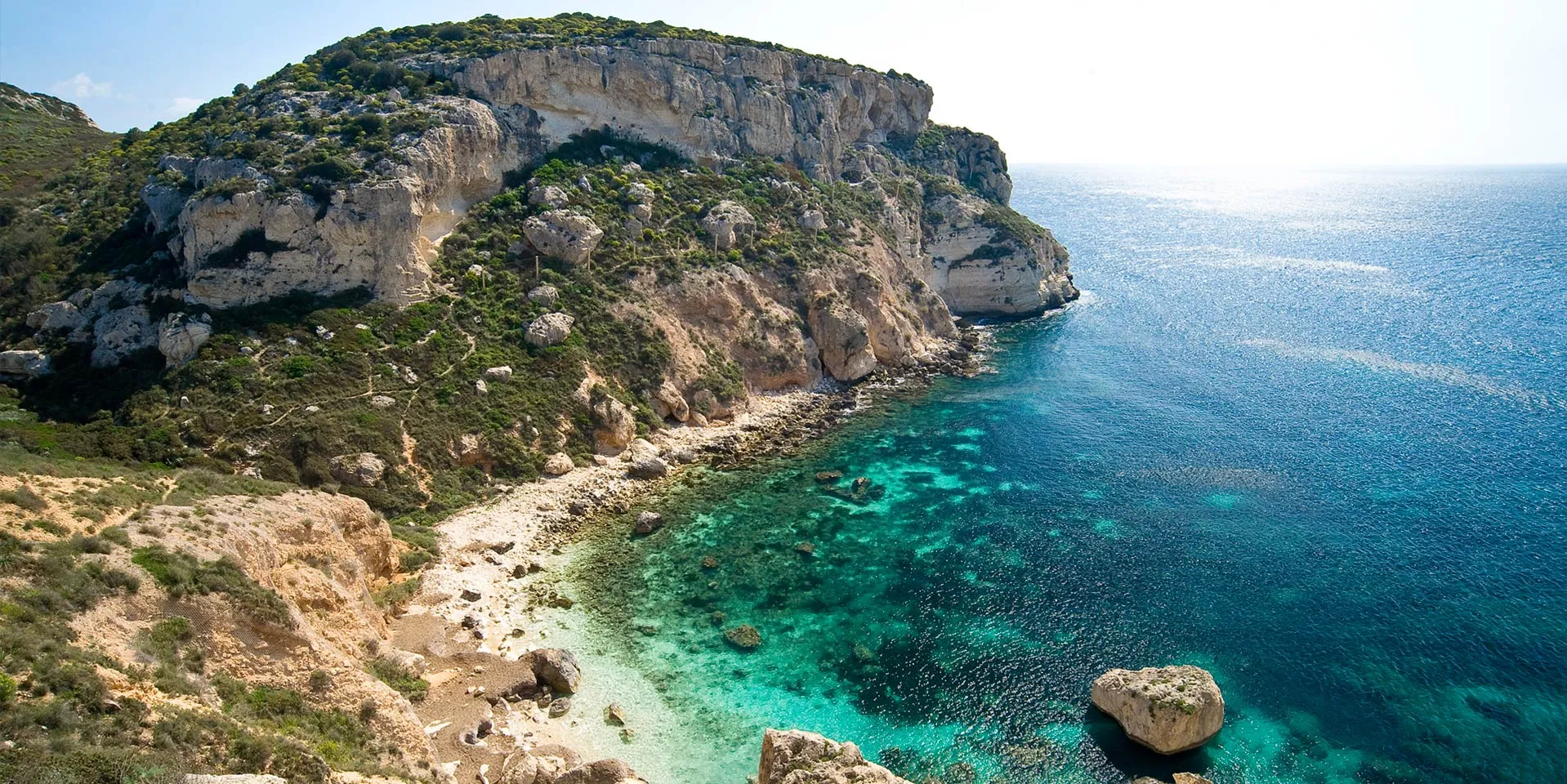 Cala Fighera, Cagliari: caletta selvaggia incastonata sotto la falesia della Sella del Diavolo, acqua turchese cristallina, accessibile a piedi tramite sentiero.