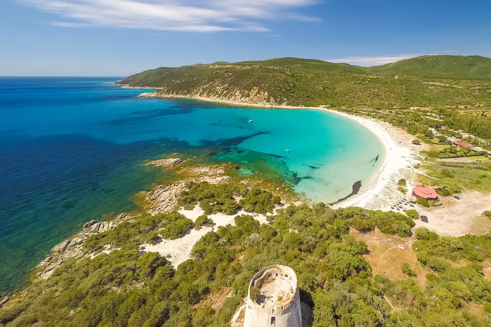 Cala Pira a Castiadas, Sardegna: piccola baia di sabbia chiara incastonata tra vegetazione mediterranea e rocce, mare cristallino dai toni turchese.