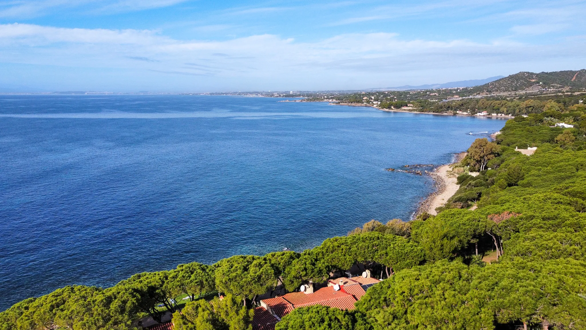 Vista aerea panoramica del Golfo di Cagliari dalla costa di Marina delle Nereidi: la città di Cagliari sullo sfondo, mare blu profondo, vegetazione mediterranea.