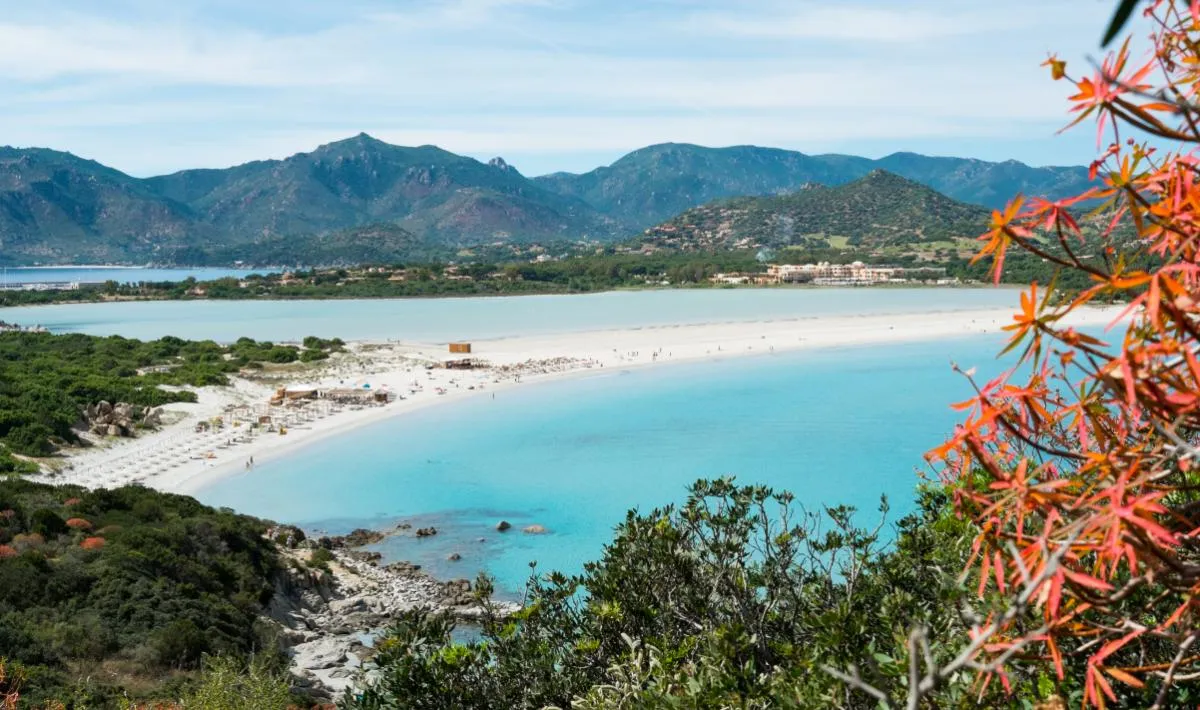 Porto Giunco a Villasimius, Sardegna: spiaggia ampia paragonata ai Caraibi per i colori che sfumano dal turchese al blu profondo, sabbia chiara e dune di vegetazione mediterranea.